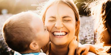 A happy mother smiling as her son kisses her cheek, illustrating the 'maternal self-efficacy' and emotional boundaries that prevent parenting burnout.