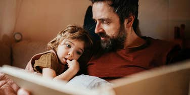 A father reading to his daughter, illustrating the 'joint attention' and emotional signaling that builds empathy in early childhood.