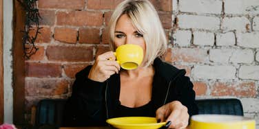 A woman with a direct, protective gaze while drinking coffee; a visual representation of the intentional stillness and exceptional boundaries shared by highly self-aware people.