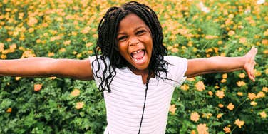 A happy child playing in a field of flowers, illustrating the 'unstructured play' and sensory integration that builds a resilient nervous system.