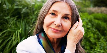 A stylish sixty-year-old woman smiling against green plants, illustrating the 'phenotypic aging' and physical vitality of a Super-Ager.