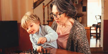 A grandmother patiently teaching her young grandson how to play chess; a visual of the deep family connection now at stake after a disagreement over daily babysitting boundaries.