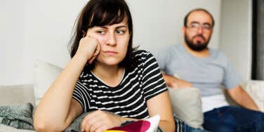 A man and woman arguing on a couch with defensive body language; illustrating the early warning signs and communication breakdowns that couples often ignore before bigger problems arise.