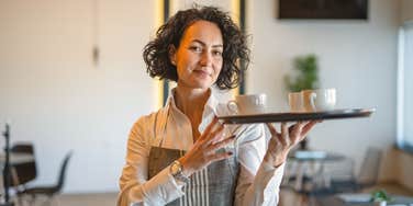 female server carrying tray with mugs
