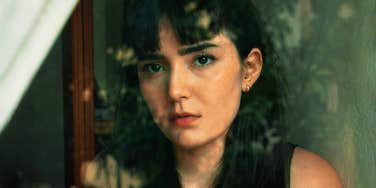 A woman looking thoughtfully out a window, capturing the internal conflict of someone who senses a repetitive pattern in their life but hasn't yet acted on it.