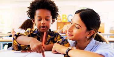 A teacher leaning in to help a student, capturing the 'emotional coaching' and the simple phrases that improve student behavior without raising a voice.