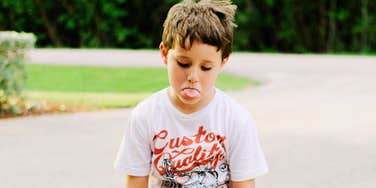 A young boy sticking out his tongue with a defiant expression, illustrating the 'emotional shutdown' and need for autonomy common in male childhood development.