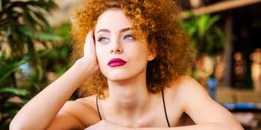 A thoughtful woman sitting at a table with a distant gaze, illustrating the signs of deep burnout that sneak up on high-functioning people