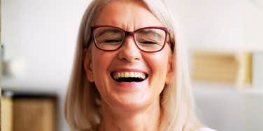 A middle-aged woman with glasses laughing candidly, illustrating the specific style of humor that a new study links to high intelligence.
