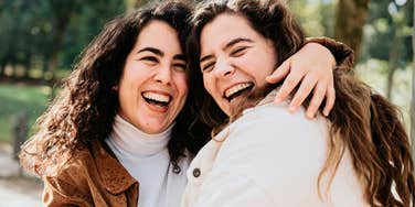 Two joyful friends laughing outside; a visual representation of the strong interpersonal bonds and loyalty that serve as an indicator of a person's intelligence.