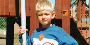 A child in a vintage Coca-Cola sweatshirt on a playground, illustrating the 'unstructured play' and boredom-tolerance skills common in the 1990s.