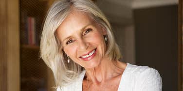 A vibrant older woman standing in a study with a warm smile, illustrating the 'ripe old age' of 66 as a time for new beginnings and professional rebirth despite past financial hardships.