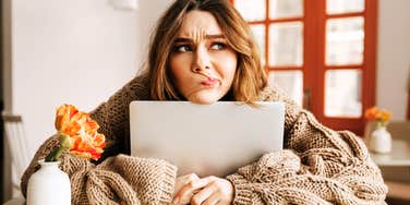 A woman in a sweater looking aside with a doubtful expression while clutching her laptop; a visual representation of the isolation and suspicion that occurs when a boss hopes an employee will quit.