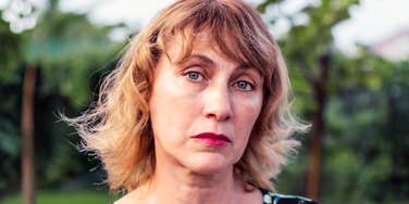 A somber middle-aged woman with blonde hair looking pensive; illustrating the "unseen" parts of getting divorced in your 50s, from social changes to the dismantling of a long-term family unit.