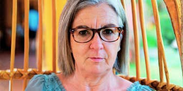 A portrait of a senior woman reflecting in a rattan chair, representing the 'estrangement surge' and the disconnect between traditional and modern parenting values.