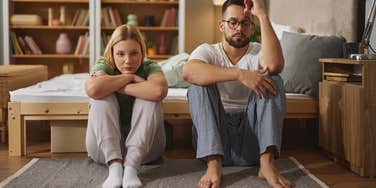 upset couple sitting next to bed on floor