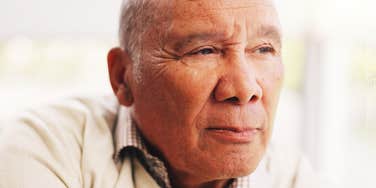 A senior man looking away with a skeptical, squinted gaze; illustrating the 'critical' father archetype and the deep-seated yearning for simple parental kindness and acceptance.