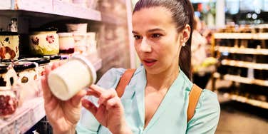A portrait of a shopper checking product prices in a grocery store; illustrating the modern 'inflation math' strategy Americans are using to decide which food staples remain worth the increased cost.