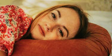 A portrait of a woman, resting comfortably on a pillow; illustrating the calm state of the body before the brain misinterprets muscle relaxation as 'falling' and triggers a sudden wake-up jerk.
