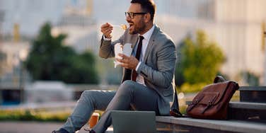 businessman eating takeout with chopsticks on steps outside