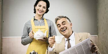 A staged vintage-style photo of a smiling woman pouring tea for her husband during breakfast; illustrating the rigid and often absurd domestic standards taught to women in the 1950s.