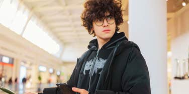 A teenage boy looking anxious and contemplative while holding his phone in a public space; illustrating the 'digital buffer' and the heightened anxiety Gen Z feels when approached by people they don't know.