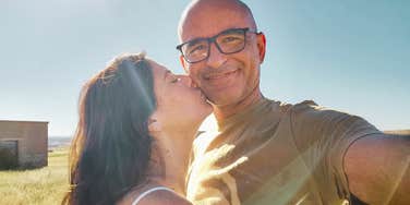 A joyful man and woman in their fifties smiling together outdoors; illustrating the deep connection and partnership found in mature relationships where different lifestyles find common ground.