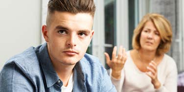Gen Z young man looking annoyed at his Gen x mom in the background