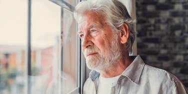 Grandparent who feels alienated from grandchildren looking out a window alone