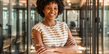 A professional Black woman posing confidently in a sleek office hallway; illustrating the connection between self-trust and the outward habits of success and happiness in a high-pressure environment.