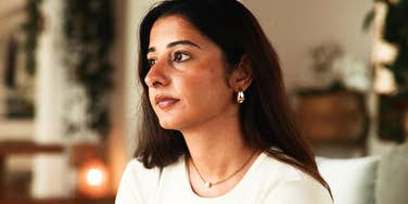 A woman in a living room looking pensive but calm; illustrating the proactive mindfulness and vision-setting happy people engage in when feeling overwhelmed by internal mental chatter.