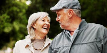 A portrait of a senior man and woman bonding and laughing outdoors; illustrating the lighthearted perspective and deep connection that keeps a marriage strong despite financial setbacks and poor investment choices.
