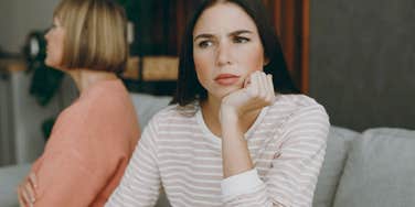 Adult daughter turned away from her mom emotionally on a couch