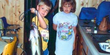 vintage photo of two kids around age 8 holding a fish while protected from harsh reality by their parents