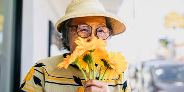A senior woman engaging her sense of smell with flowers in a garden; illustrating the 'odd' multisensory exercises—like olfactory training—that allow 'Super-Agers' to maintain younger brain function.