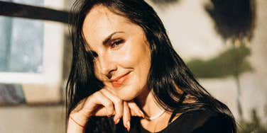 A happy woman basking in the sun in an old-world city setting; illustrating the transition from 'external validation' to 'internal authority' and how letting go of societal expectations can radically improve a woman's quality of life.