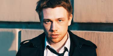 A blonde man in a suit looking away from the camera with a guarded expression; illustrating the 'performative confidence' and subtle social cues that experts identify as red flags for lack of integrity.