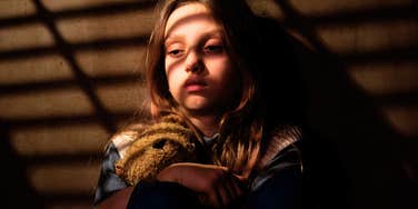 A sad girl leaning against a wall, partially obscured by shadows; a visual representation of the 'narcissistic paradox' where a child feels smothered by parental control yet completely abandoned emotionally.
