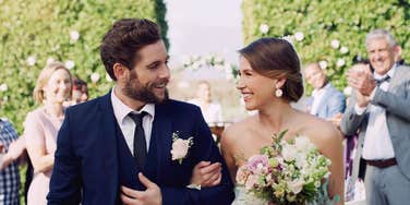 married couple walking down aisle at wedding with family standing behind them