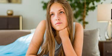 A portrait of a young teenager lying on a couch with a pensive and detached expression; illustrating the common developmental phase where thirteen-year-old girls seek solitude and exhibit cat-like social boundaries.