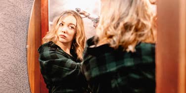 A woman preparing to go out and focusing on her appearance in the mirror; illustrating the surprisingly personal connection between how we curate our image and our internal state of happiness.