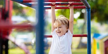 little boy climbing on bars at park outside