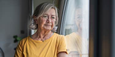 elderly woman standing next to window