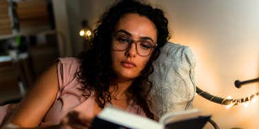 A young woman in glasses immersed in a novel in a cozy bedroom with warm string lights; a visual representation of the 'reading rituals' and focused habits that allow high-volume readers to finish more books than average.