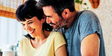 A happy couple sharing a candid, joyful moment in their kitchen; illustrating the 'secure attachment' and shared laughter that experts say are the foundational behaviors of a sustainable, life-long partnership.