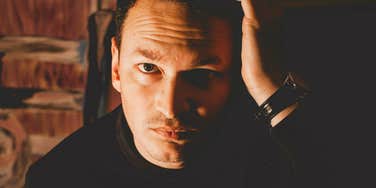 A man with a dark, serious, and intense expression in low-light photography; illustrating the paradoxical relationship between perceived reliability and the 'shadow side' of high-trust personalities.
