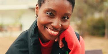 A friendly portrait of a woman with a backpack smiling in the sun; illustrating the approachable yet resilient nature of people who use specific daily phrases to stay calm and unbothered by life’s drama.