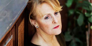 A mature woman standing against a wall looking pensive and concerned; illustrating how behaviors often viewed as negative, such as avoidance or compartmentalization, can offer vital emotional protection in specific contexts.