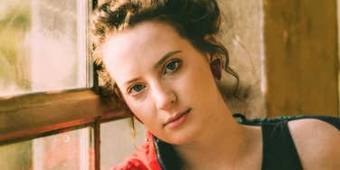 Quiet young woman by a window likely had a painful childhood