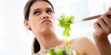 A woman contemplating her meal with a puzzled expression while eating a salad; illustrating the 'palate fatigue' and biological factors that can prevent someone from tasting the full profile of their food.